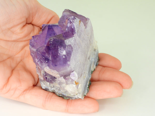 Beautiful Amethyst cluster with inclusions in someone's hand. Other side view